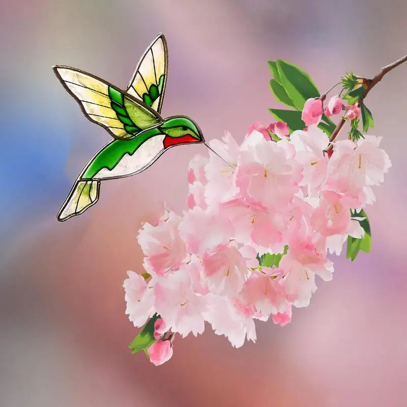 Stained glass hummingbird hovering near pink cherry blossoms against a softly blurred, colorful background.