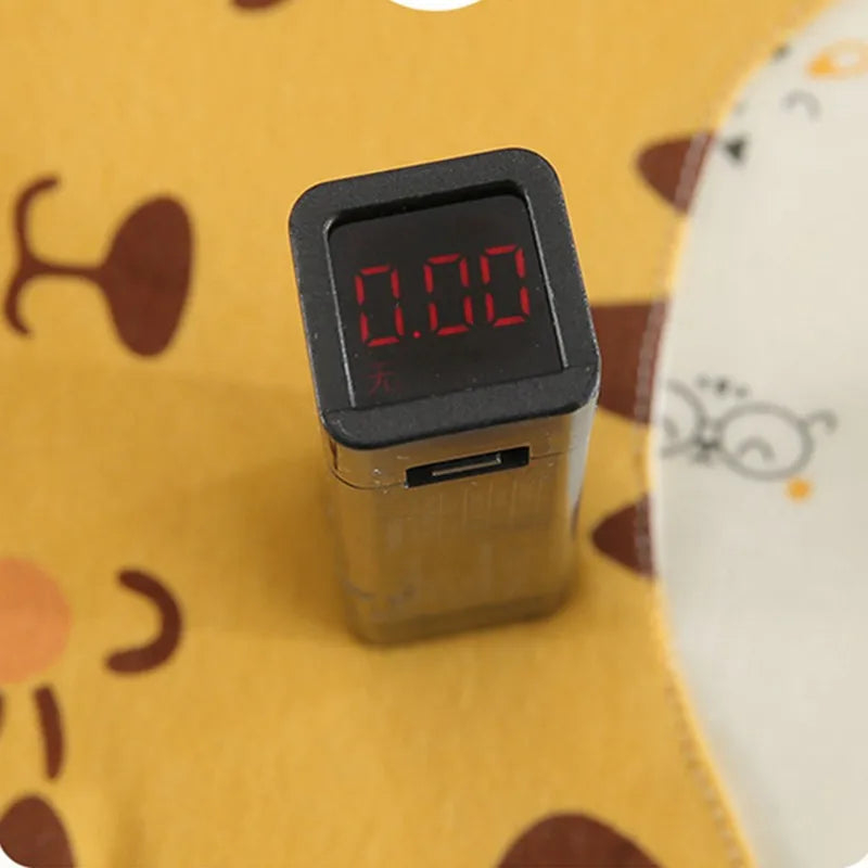 Digital display device with a red "0.00" reading on a black square screen. It's set on a yellow surface with abstract brown and white patterns featuring glasses and circles.