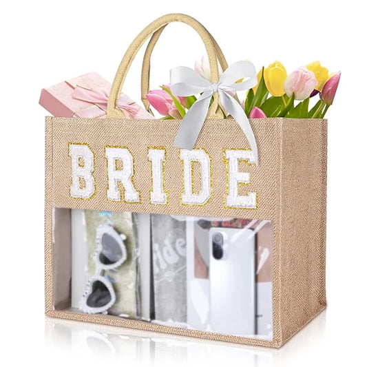 A beige tote bag with "BRIDE" in white letters, a white bow, and filled with tulips, a pink gift box, sunglasses, and a smartphone, displayed creatively.
