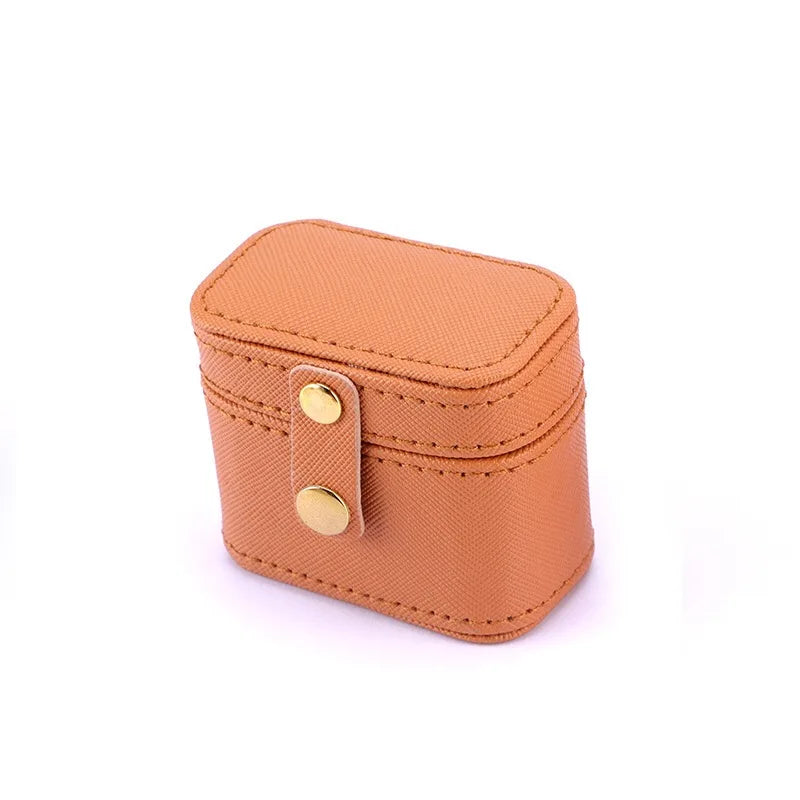 Small tan rectangular leather case with rounded edges. It features a lid secured by a strap with two gold-tone snap buttons. The stitching is visible and matches the color of the leather.