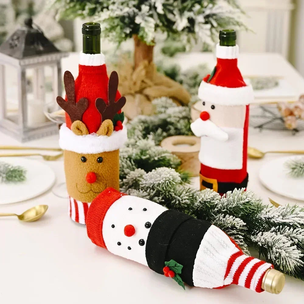 Festive wine bottles in holiday-themed covers: reindeer, snowman, and Santa, on a decorated table with greenery and a tree. Lantern and plates visible in the background.