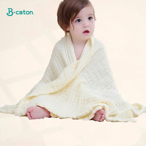 A baby sits wrapped in a soft, cream-colored blanket with a curious expression. The background is plain, and the logo "B-caton" is visible in the top left corner.