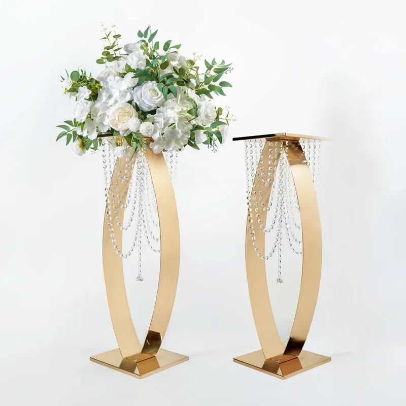 Elegant gold stands with cascading crystal beads; one topped with lush white flowers and greenery, the other empty, against a plain background.
