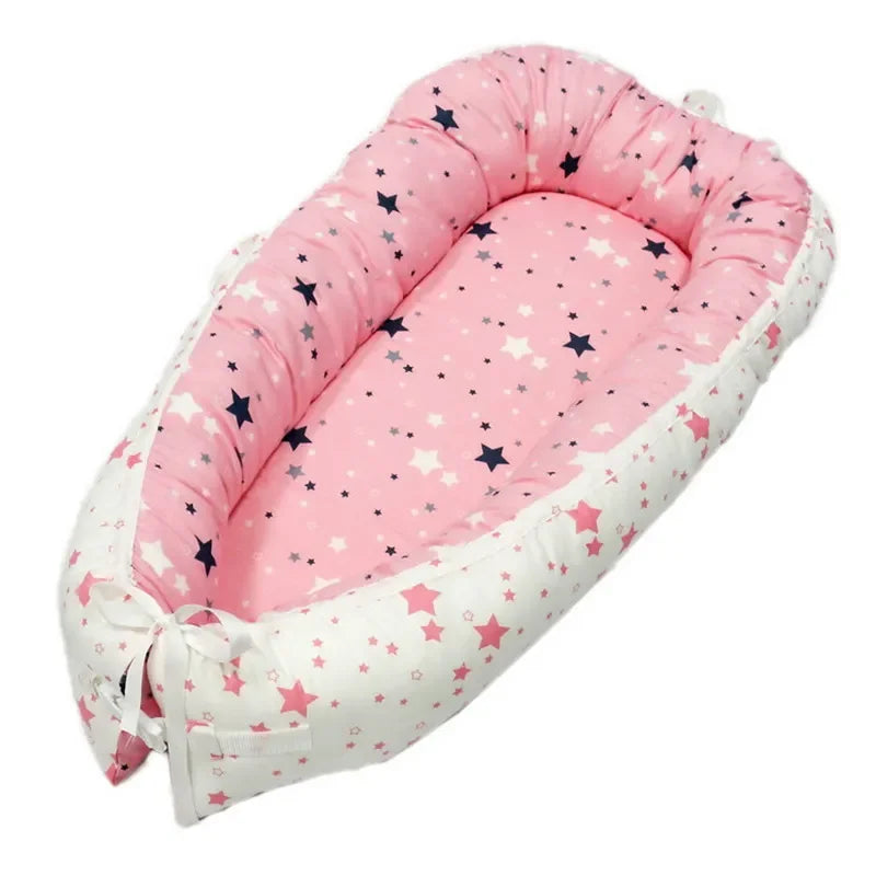 Pink and white baby nest with a star pattern, featuring a cushioned border and tied ends. The inner pink area is adorned with small navy and gray stars.
