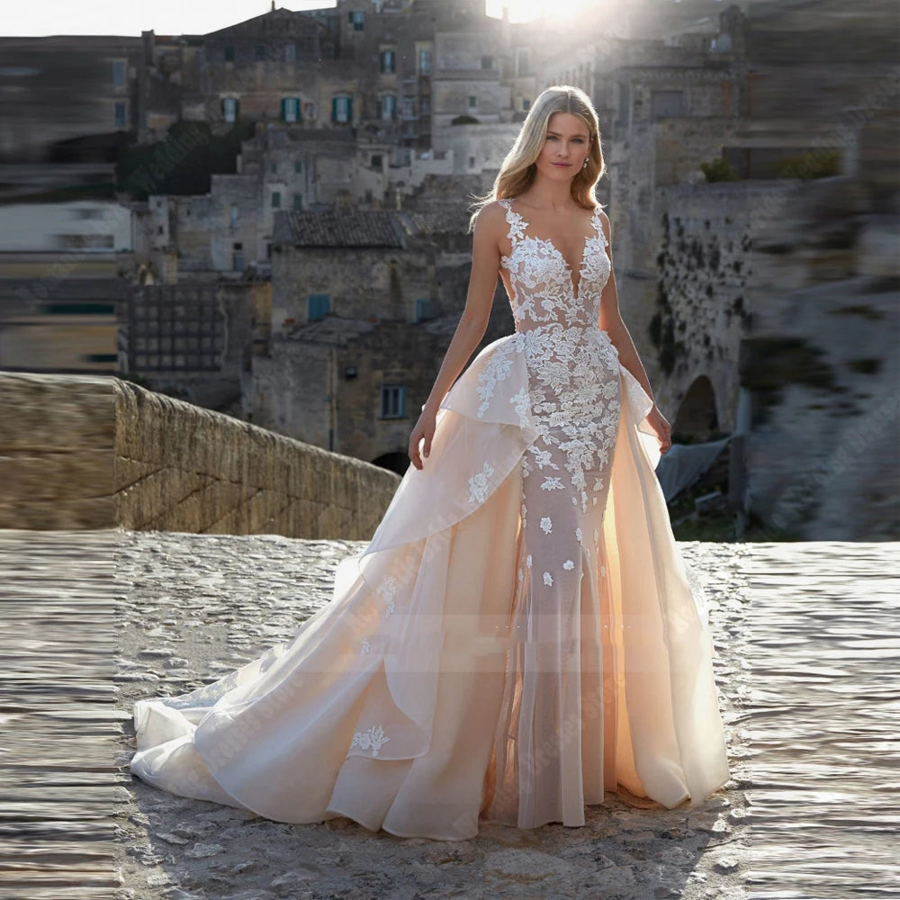 A woman in a flowing, lace-adorned gown stands on a sunlit stone path, with an ancient stone building in the background capturing an ethereal, romantic ambiance.