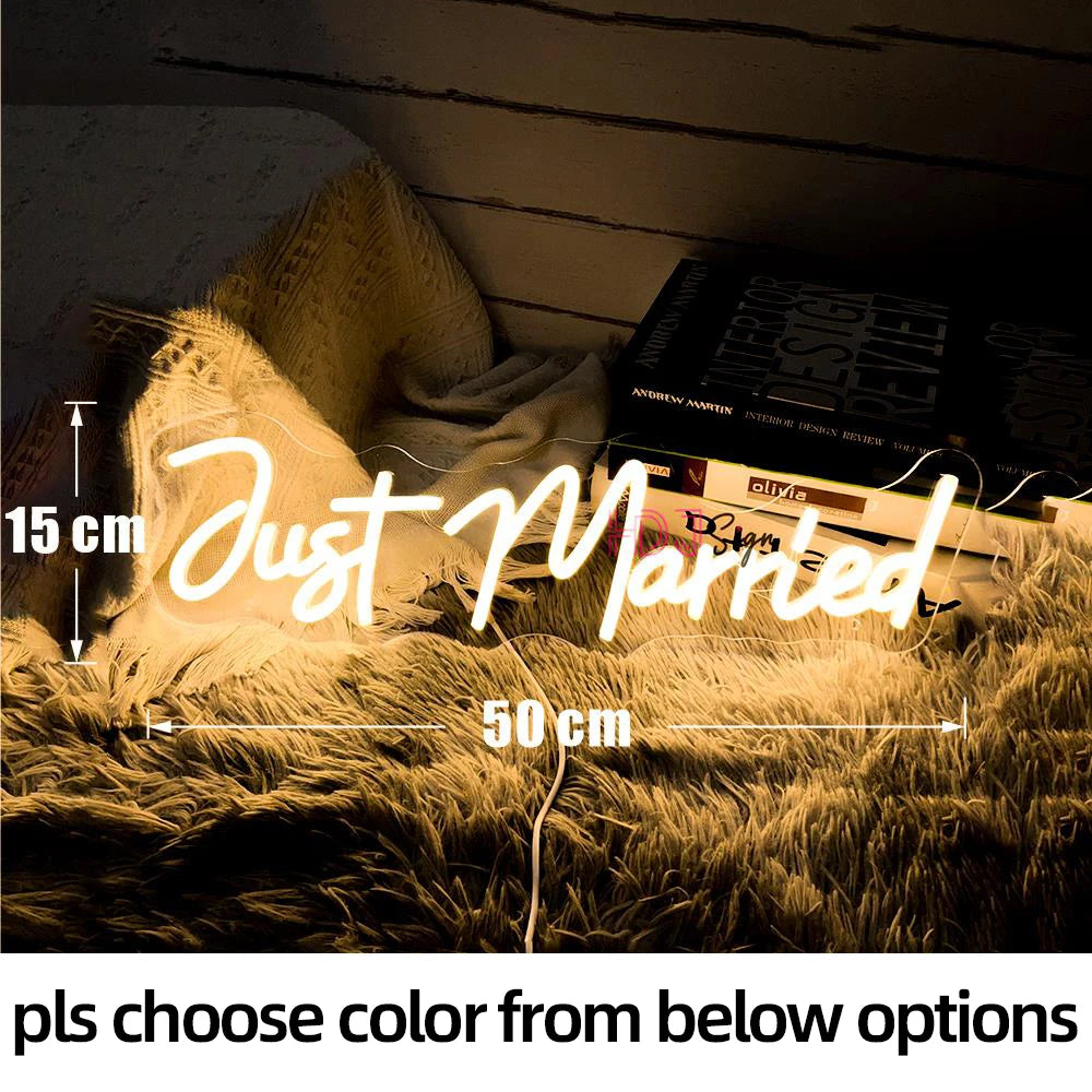 Neon sign reading "Just Married" in cursive, measuring 15 cm high and 50 cm wide, lying on a textured blanket with books nearby. Text below reads "pls choose color from below options."
