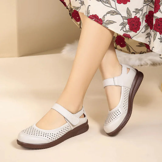 A person wearing white perforated Mary Jane shoes with brown soles, paired with a floral skirt featuring red and black flowers.