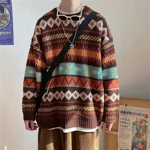 Person wearing a colorful, patterned sweater with browns, oranges, and blues. They have a shoulder bag, necklace, and sunglasses on their neck. Background includes a poster and a framed print.