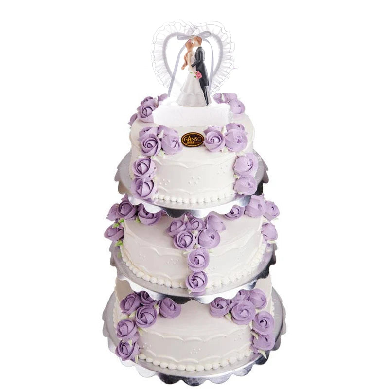 Three-tier white wedding cake adorned with purple rose decorations. A bride and groom figurine stands on top beneath a heart-shaped frame.