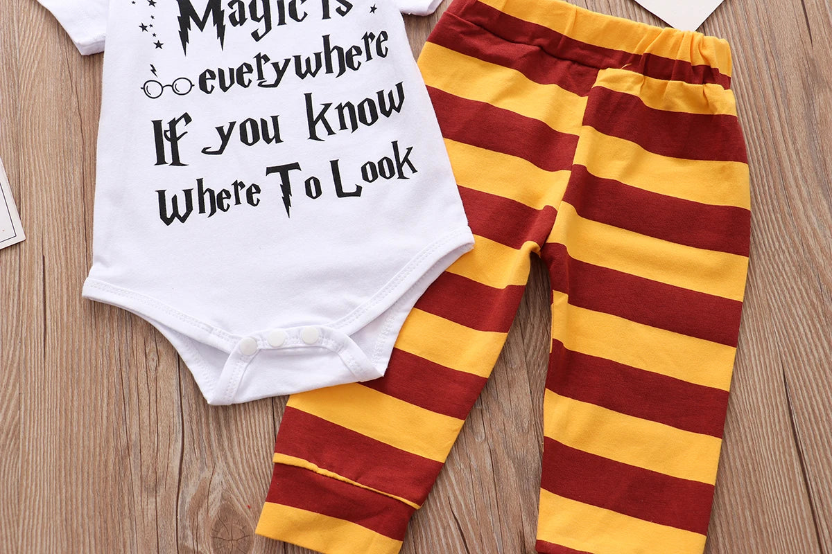 White baby onesie with "Magic is everywhere if you know where to look" in black print, next to red and yellow striped pants, on a wooden surface.
