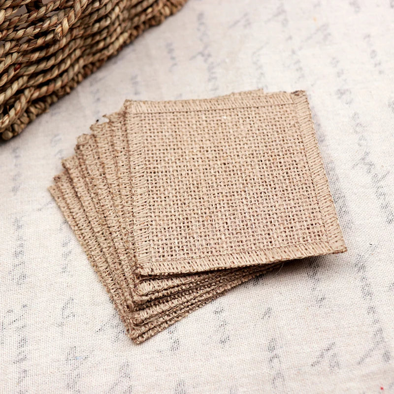 Stack of square burlap coasters on a lightly patterned fabric surface, with part of a woven basket visible in the corner.