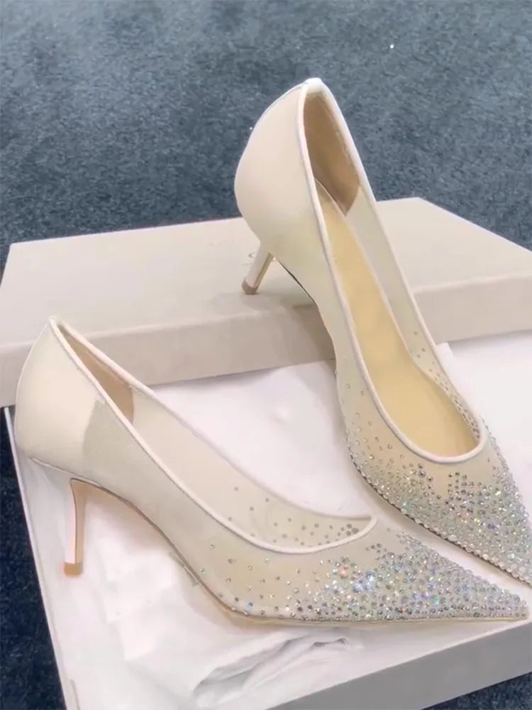 Elegant white high heels with pointed toes, adorned with sparkling rhinestones, displayed on a white shoebox against a blue carpet background.