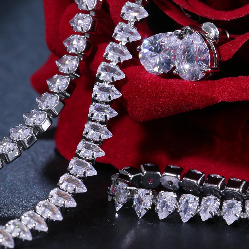 Elegant silver jewelry with pear-shaped gemstones on red velvet fabric, showcasing a bracelet and earrings with sparkling stones on a dark surface.