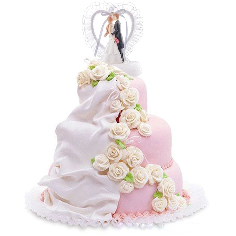 A three-tiered pink wedding cake decorated with cascading white roses and fabric, topped with a bride and groom figure inside a frilled heart.