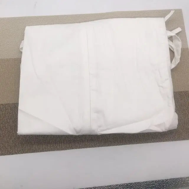 Folded white apron with ties, placed on a striped beige and gray mat. The apron appears clean and neatly arranged.