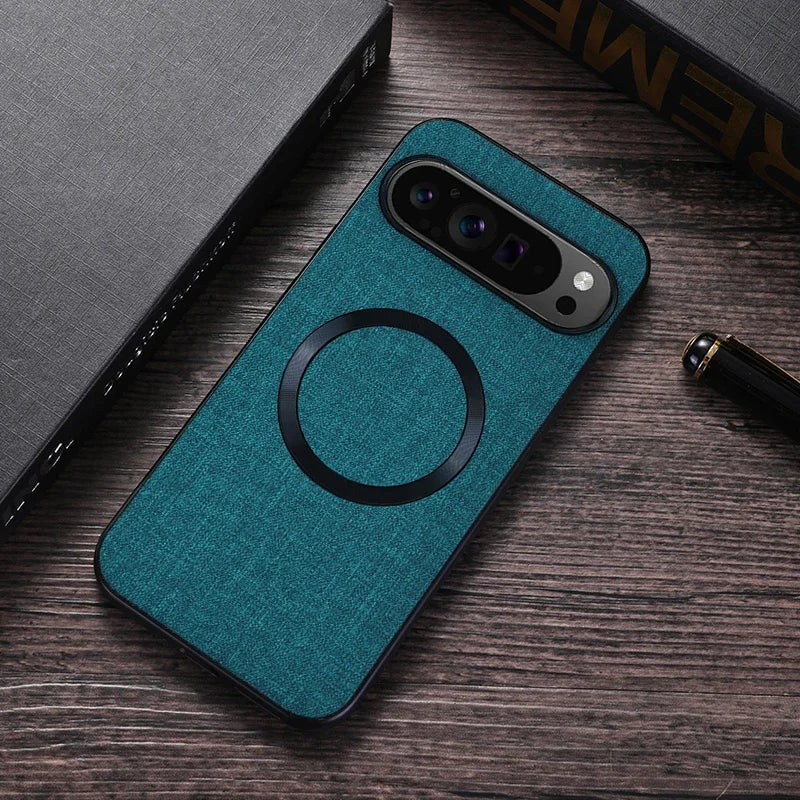 Teal fabric-textured phone case with a black ring design, placed on a wooden surface beside a closed book and a pen. The phone's camera lens is visible.