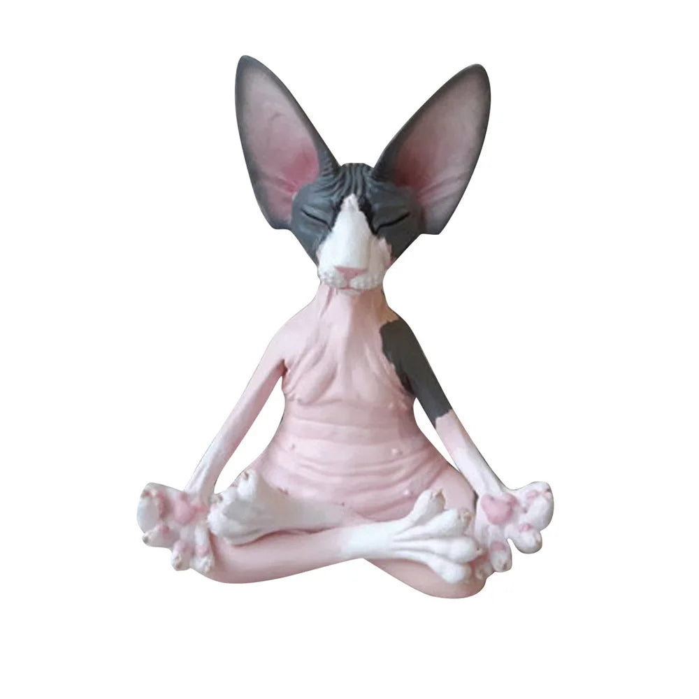 A ceramic figure of a hairless cat meditating in a lotus position. The cat has closed eyes, a pink and gray body, large ears, and is set against a white background.
