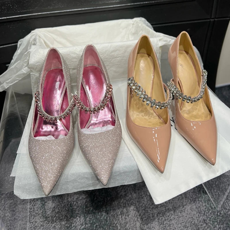 Two pairs of elegant women's heels are displayed. One pair is glittery silver with pink insoles, and the other is glossy beige. Both feature decorative jeweled straps.
