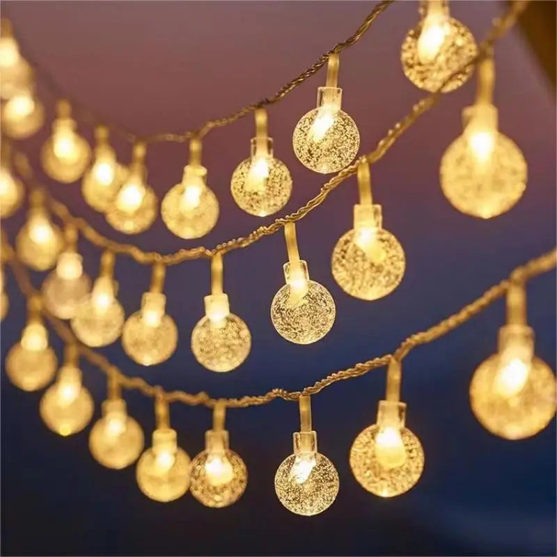 A string of glowing round fairy lights with a textured surface hangs across a blurred dark background, creating a warm, festive ambiance.