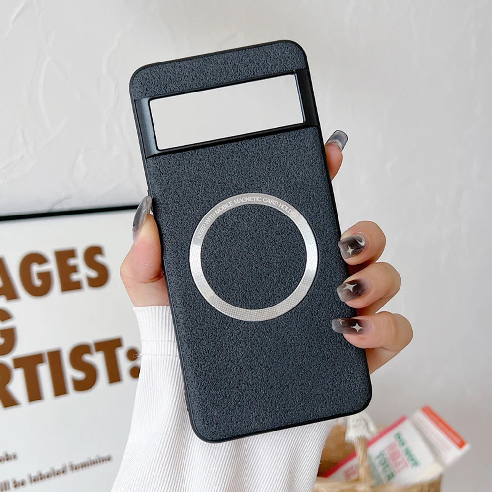 A hand holds a black phone case with a silver magnetic ring and card holder slot. The background shows a blurred wall with framed text and a box of items.