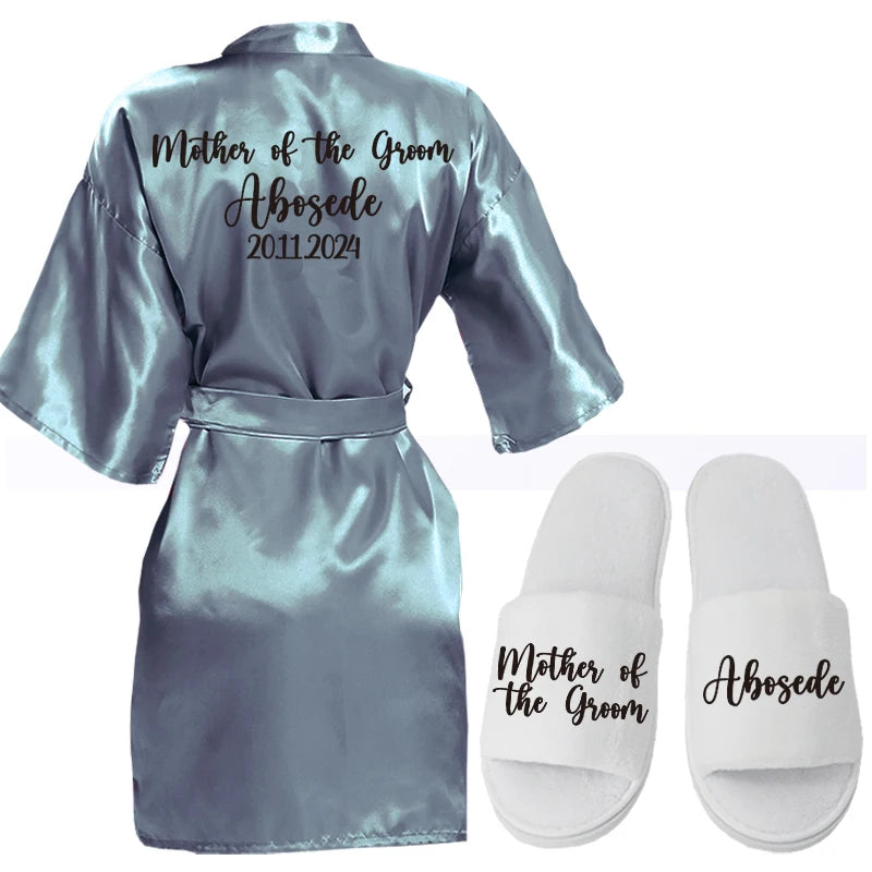 Silver satin robe with "Mother of the Groom" and "Abosede 2011-2024" printed on the back. Paired white slippers feature similar text.