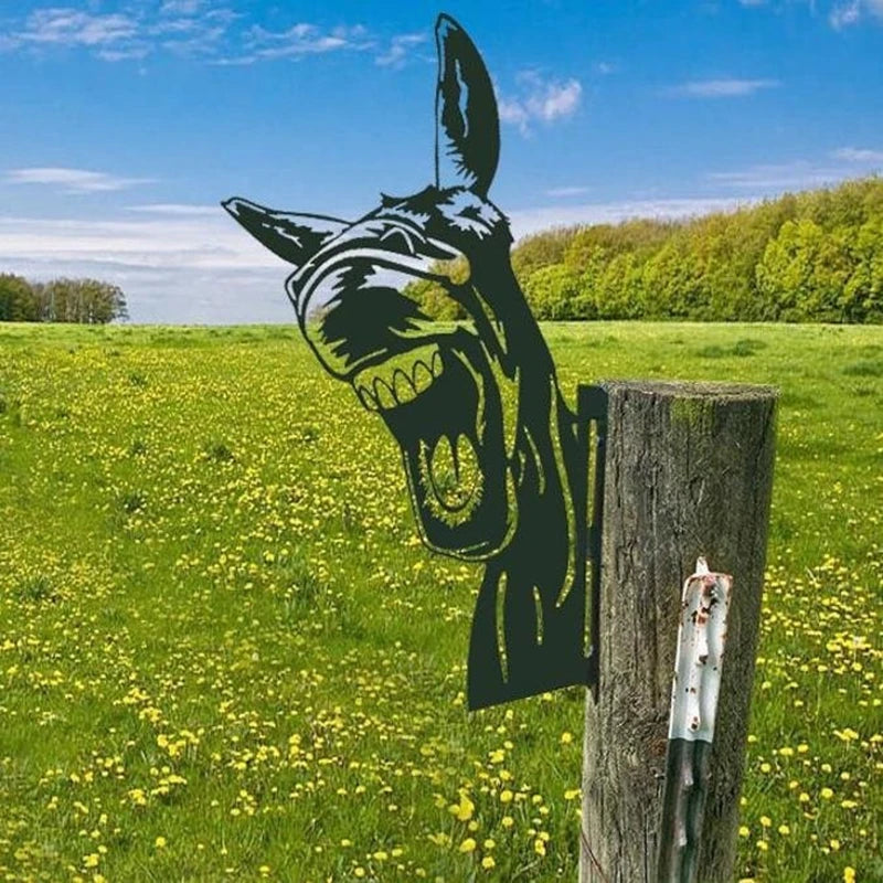 A metal silhouette of a laughing donkey is attached to a wooden post in a field of yellow flowers under a blue sky.