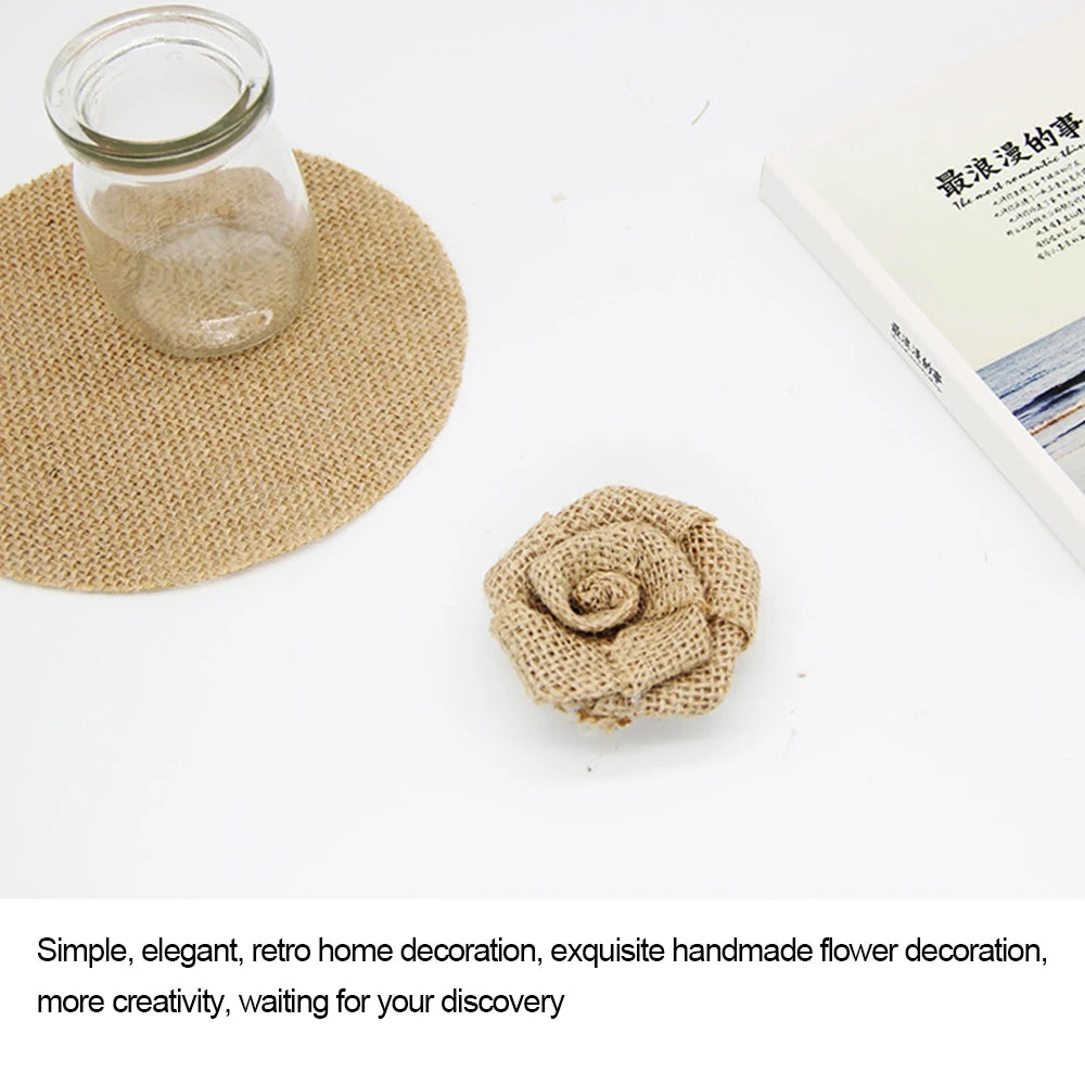 A burlap jar coaster next to a matching burlap rose on a white surface, with a corner of a book visible, creating a simple and elegant decor arrangement.