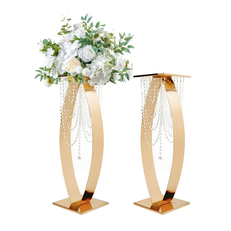 Gold flower stands with crystal bead drapes, featuring one adorned with white and cream flowers and green leaves, and the other empty, both on square bases.