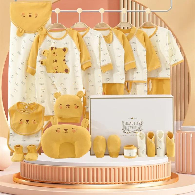 A baby clothing set displayed on hangers includes bear-themed garments and accessories in beige and mustard colors, with a matching pillow and decorative box on a round stand.