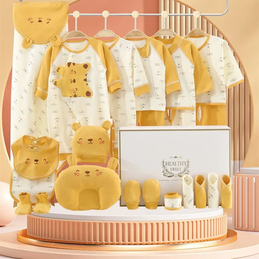 A baby clothing set displayed on hangers includes bear-themed garments and accessories in beige and mustard colors, with a matching pillow and decorative box on a round stand.