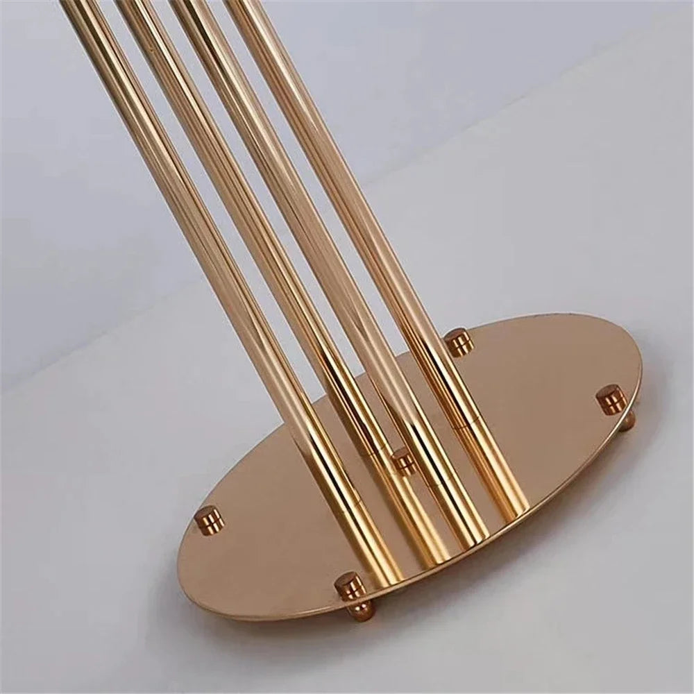 Close-up of a shiny gold metal stand with multiple vertical rods attached to an oval base, placed on a white surface with a minimalistic design.