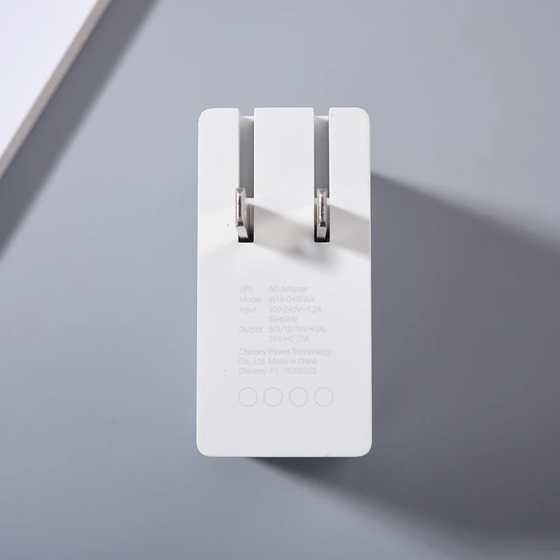 White power adapter standing upright on a gray surface, showing model number and specifications for input and output. The prongs are folded in, and light casts a soft shadow.