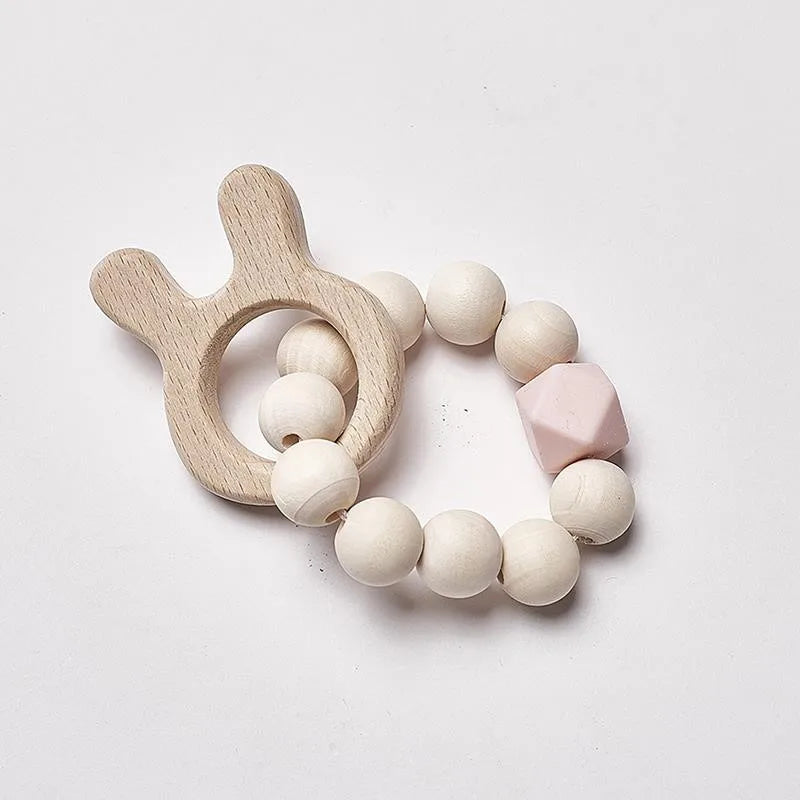 Wooden teething ring with round beads and a pink hexagonal bead. It features a bunny-shaped wooden handle, designed for infants to grasp and chew.