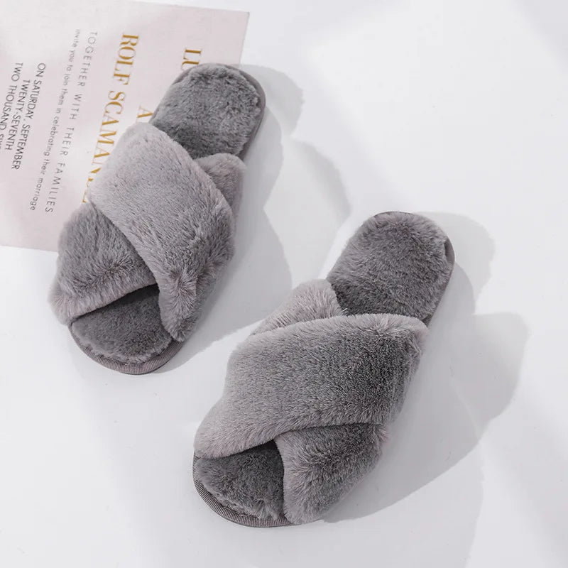 Gray fuzzy slippers with crisscross straps on a white surface. A piece of text in the background, partially obscured by the slippers, adds a casual, cozy vibe.
