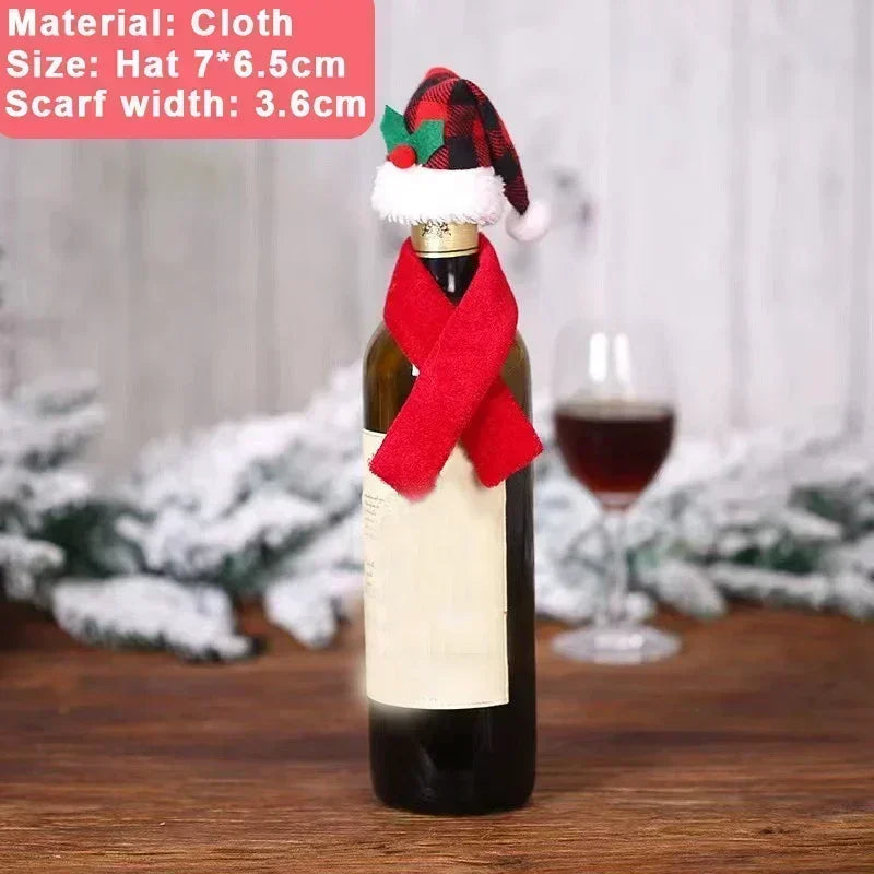 Wine bottle dressed in a red festive scarf and black-red plaid Santa hat, placed on a wooden table with snow-covered greenery and a glass of wine in the background.
