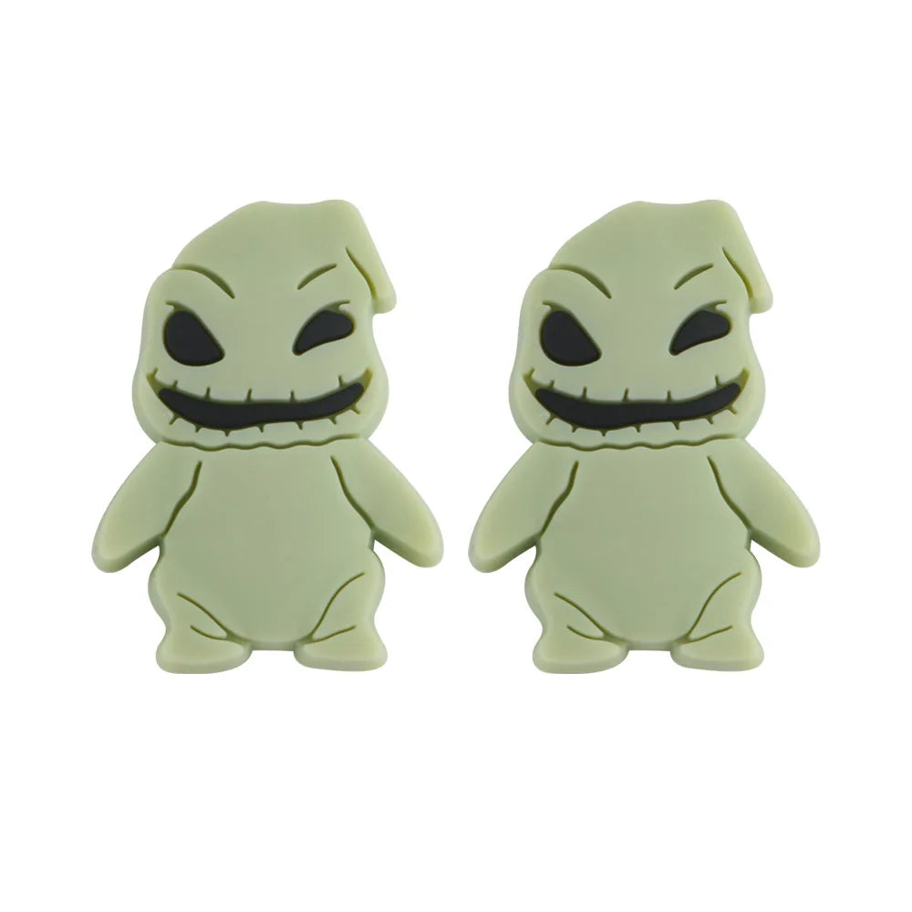 Two identical green cartoon figures with stitched smiles and black eyes, resembling spooky characters. They have rounded bodies, small legs, and pointed head crests.