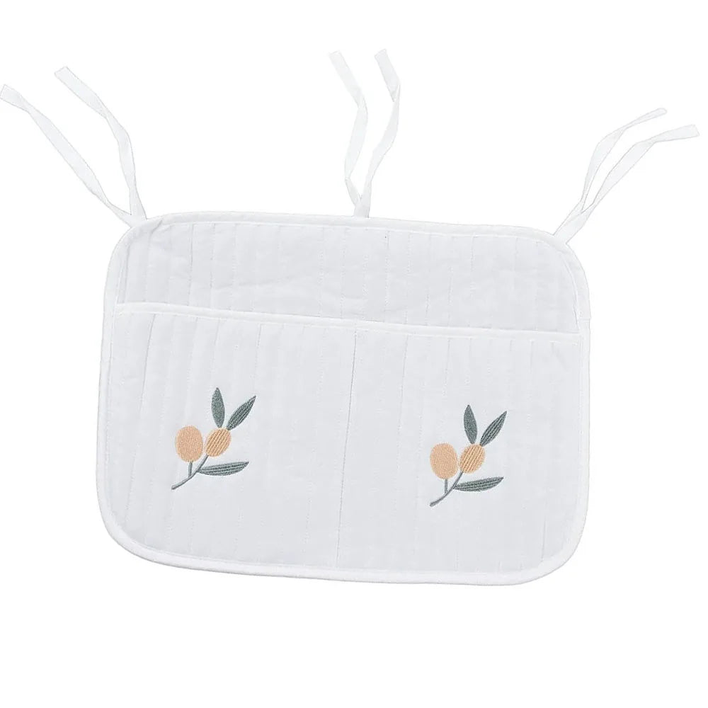 White cushioned seat pad with two vertical pockets and delicate floral embroidery. It features ties for attachment, with soft textures and a simple, elegant design.