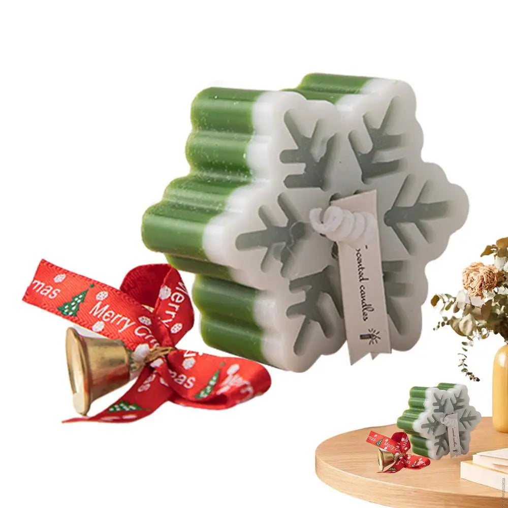 Green and white snowflake-shaped scented candle with a tag, placed near a small gold bell tied with a red "Merry Christmas" ribbon, on a wooden surface.