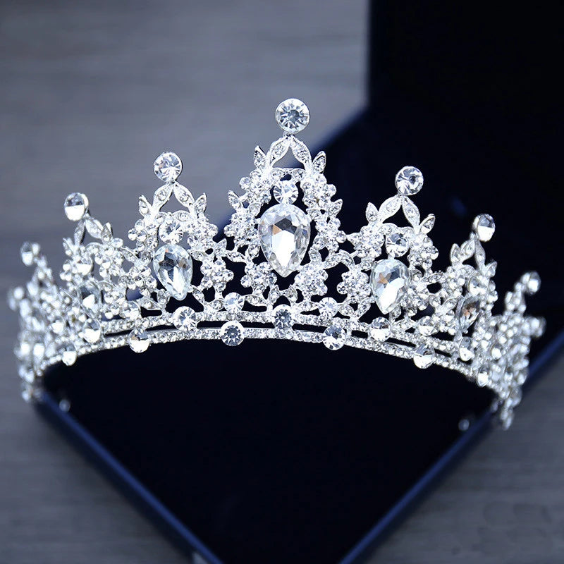 A sparkling silver tiara encrusted with large teardrop-shaped and round diamonds rests in an open black box, showcasing its intricate floral design and elegant craftsmanship.