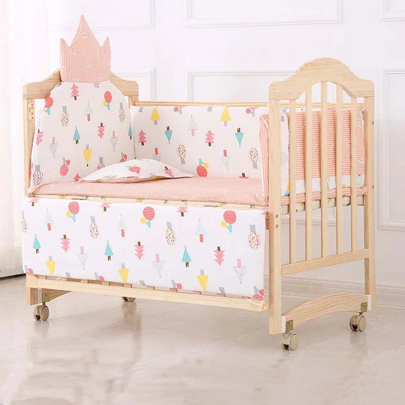 Wooden baby crib with pastel cushion set adorned with colorful geometric patterns and a crown-shaped headboard cushion. The crib has wheels for easy mobility.