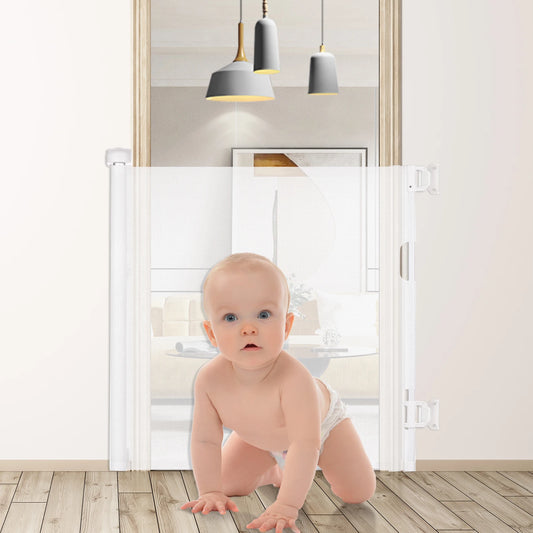 A baby in a diaper crawls on a wooden floor in front of a white retractable safety gate, with modern pendant lights hanging in the background.