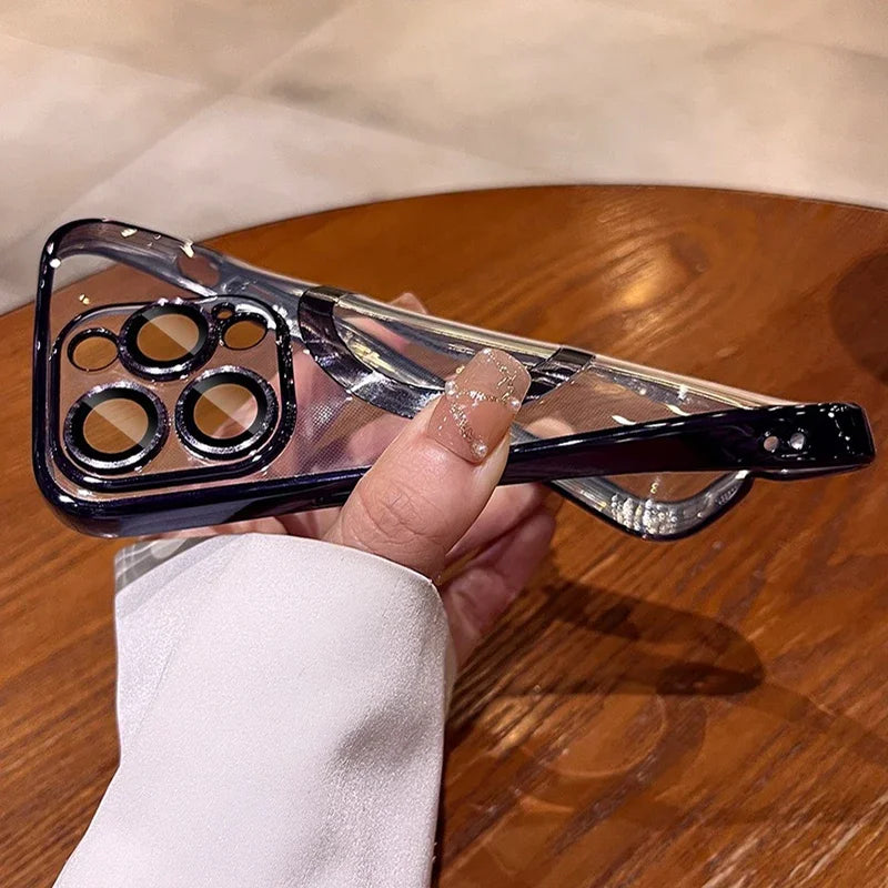 A clear phone case with metallic accents is held by a person with glittery nail art, positioned over a wooden table.