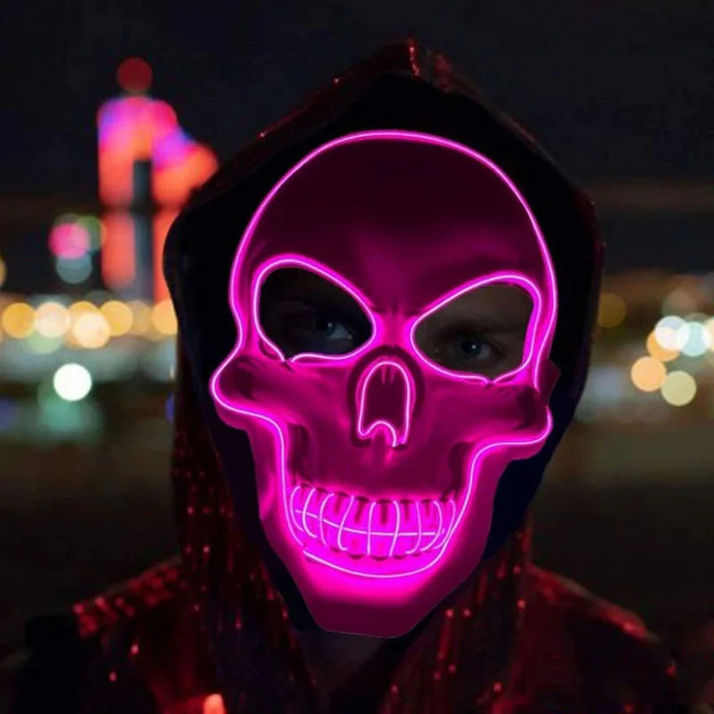 Person wearing a glowing pink neon skull mask in a dark urban setting with blurred colorful lights in the background.