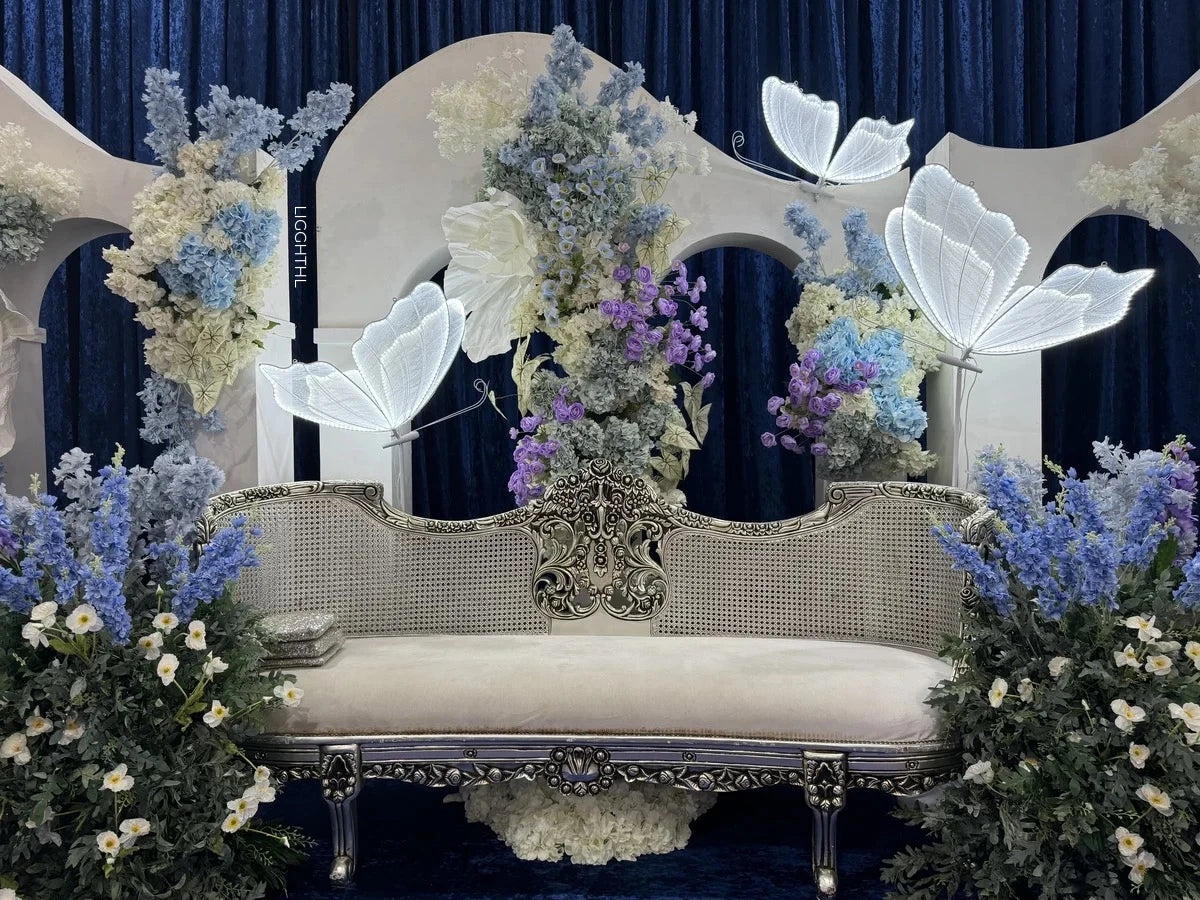 Elegant vintage bench adorned with intricate designs, surrounded by pastel flowers and ethereal white butterfly decorations against a deep blue curtain backdrop.