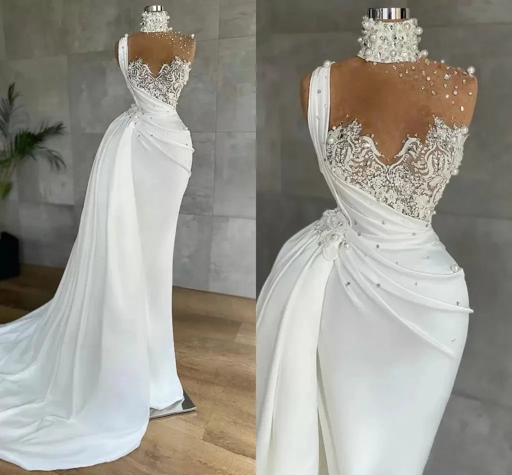 Elegant white gown on a mannequin, featuring intricate lace and pearl detailing on the bodice and shoulders, with a flowing skirt and a sleek choker-style neckline.