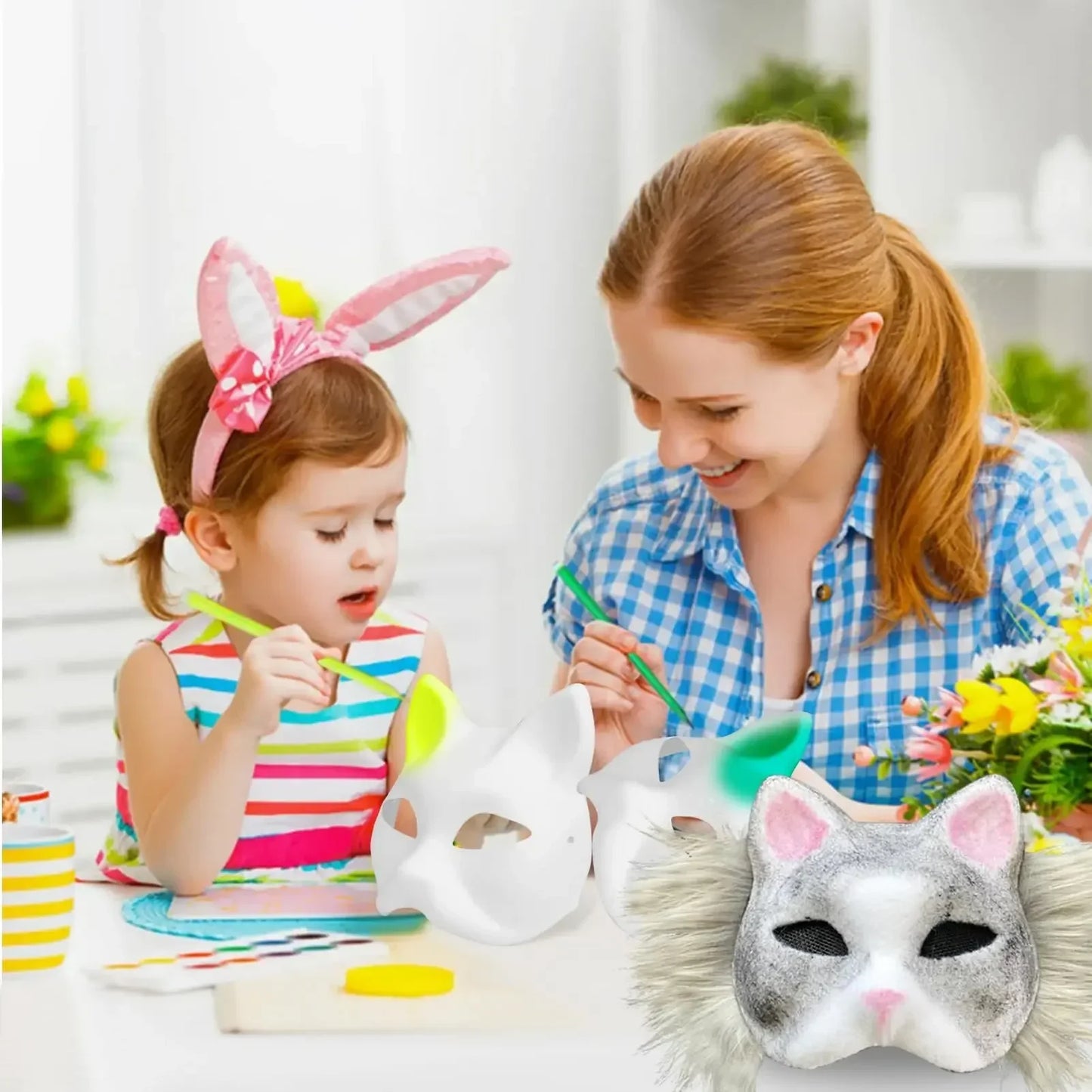 A mother and daughter paint animal masks together at a table. The girl wears bunny ears, and colorful masks lie in front of them. A vase of flowers is in the background.