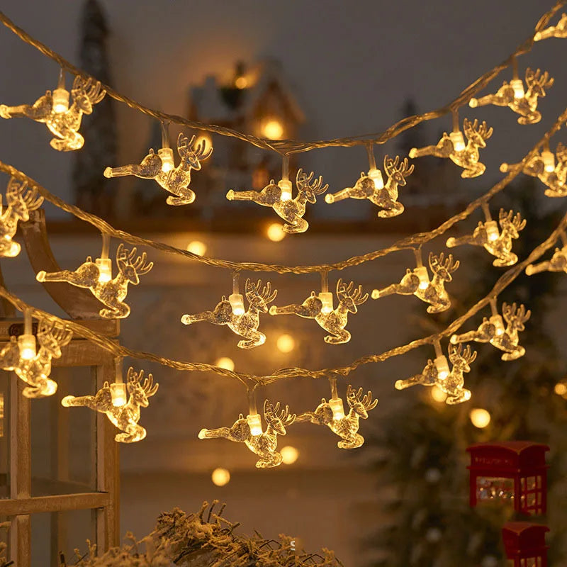 Strings of reindeer-shaped lights glow warmly, hanging in a festive outdoor setting with blurred holiday decorations in the background, creating a cozy Christmas atmosphere.