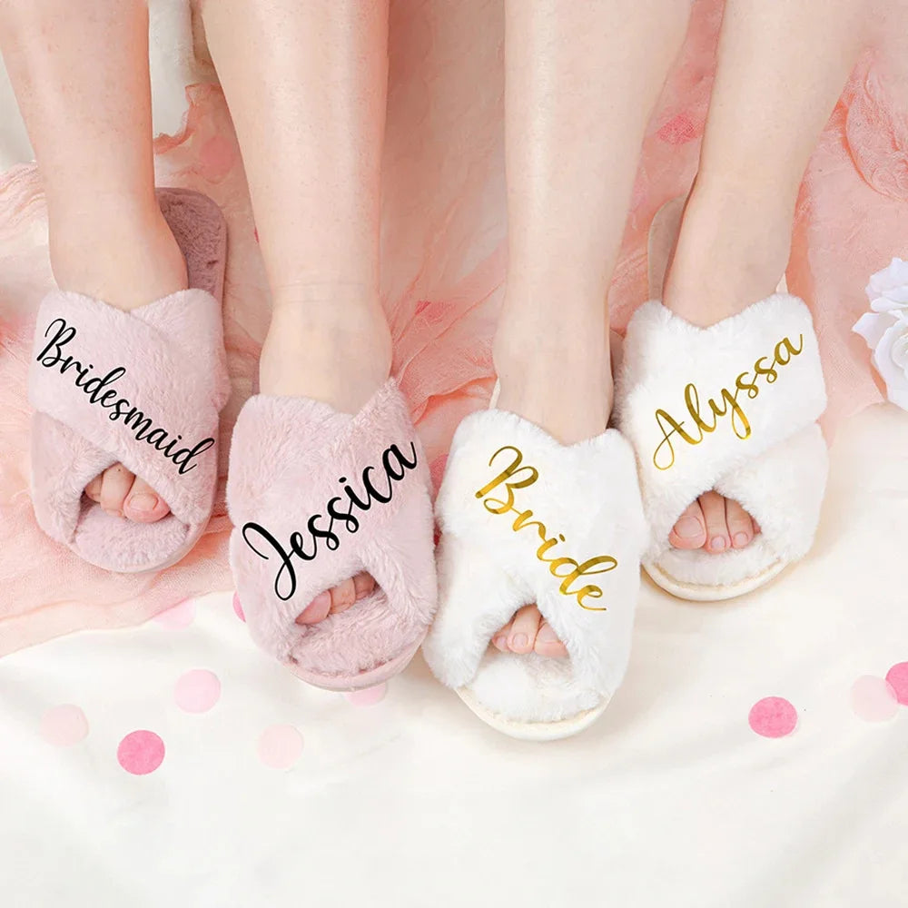 Three pairs of fuzzy slippers with names written on them: "Bridesmaid" and "Jessica" on pink, "Bride" and "Alyssa" on white. They rest on a pink and white background.