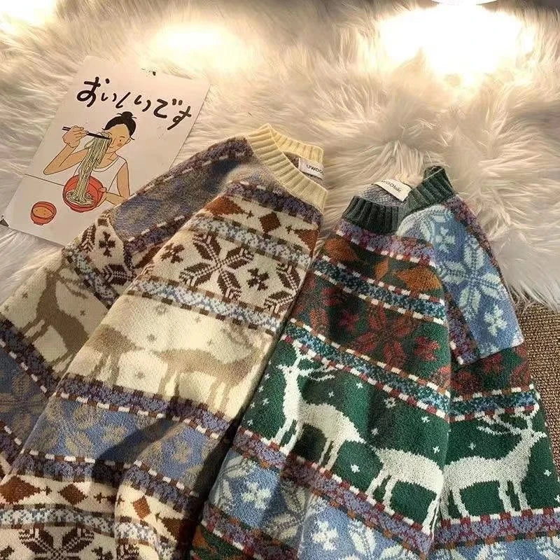 Two cozy sweaters with deer and snowflake patterns in cream and green lay on a fluffy white surface next to a Japanese noodle-themed postcard.