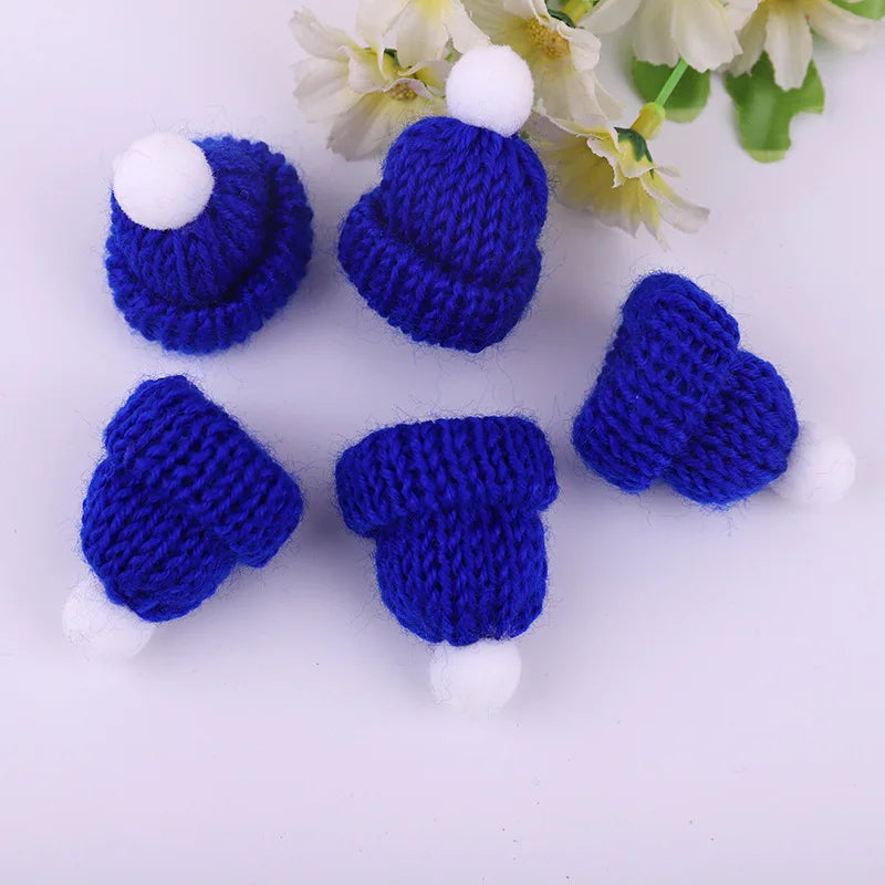 Five tiny blue knit hats with white pom-poms arranged on a white surface, accompanied by delicate white flowers in the background.